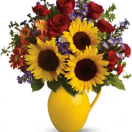 Sunflowers and red roses in a yellow pitcher vase