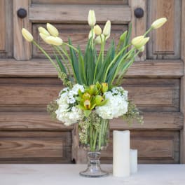 White tulips and hydrangeas in a clear glass vase with two candles