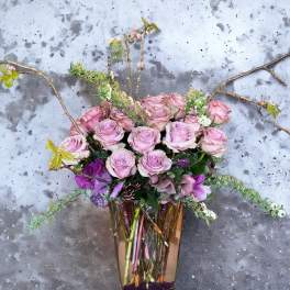 Pink roses and purple flowers arranged in a tall glass vase