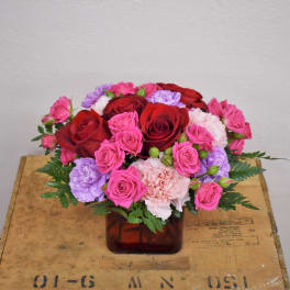 Bouquet of red, pink, and lavender flowers in a square glass vase