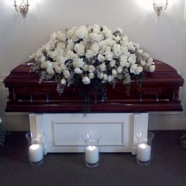White rose casket spray with candles around a wooden casket