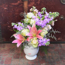 Pink lilies and purple flowers arranged in a white face vase