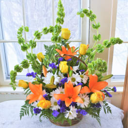 Basket arrangement of orange lilies, yellow roses, and white daisies