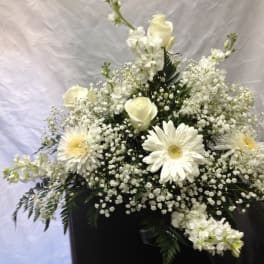 White floral arrangement with roses and daisies in a dark container