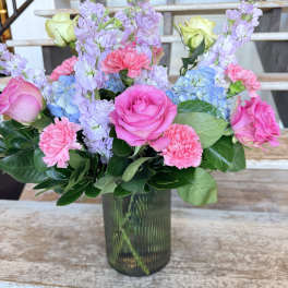 Pink roses, lavender blooms, and blue hydrangeas in a glass vase