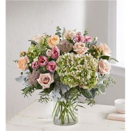 Mixed bouquet of roses, hydrangeas, and pink blooms in a glass vase