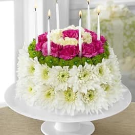 Tiered floral cake with white daisies, pink carnations, and candles