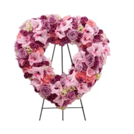 Heart-shaped floral wreath in pink and purple tones on a black stand