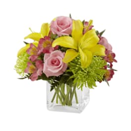 Pink roses and yellow lilies in a clear square vase