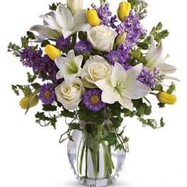 Bouquet of white lilies, roses, and purple flowers in a glass vase