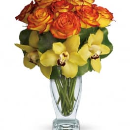 Orange and yellow roses with yellow orchids in a clear glass vase