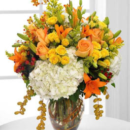 Bouquet of orange lilies, yellow roses, and white hydrangeas in a glass vase