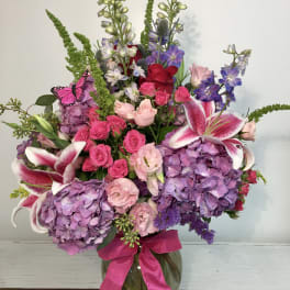 Large bouquet of pink, purple, and white flowers in a glass vase with a ribbon