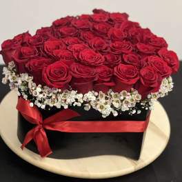 Red roses arranged in a black box with a red ribbon