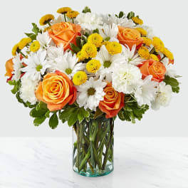 Bouquet of orange roses, white daisies, and yellow button flowers in a glass vase