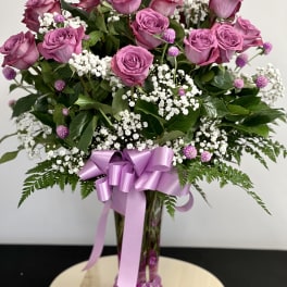 Pink roses with baby's breath in a clear vase, tied with a lavender ribbon