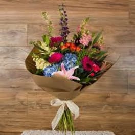 Mixed bouquet of colorful flowers wrapped in brown paper with a white ribbon