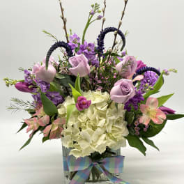 Lavender roses and purple flowers in a glass vase with a plaid ribbon