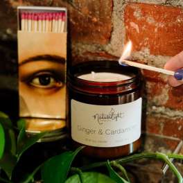 Amber jar ginger and cardamom candle being lit with a match beside a matchbox.