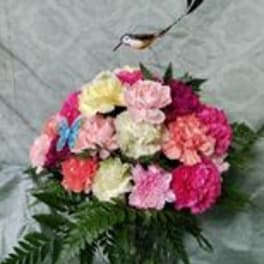 Colorful bouquet of carnations in a glass vase with a bird ornament above