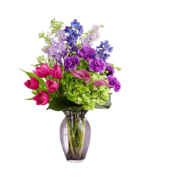 Colorful bouquet of tulips, hydrangeas, and purple flowers in a glass vase