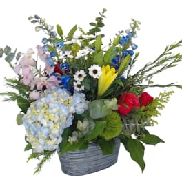 Mixed flower arrangement in a gray container with blue, pink, yellow, and red blooms
