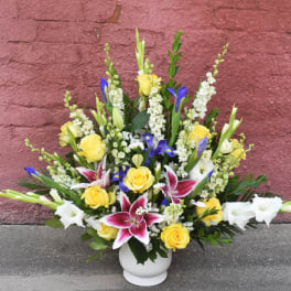 Mixed bouquet of yellow roses, white lilies, and blue irises in a white vase