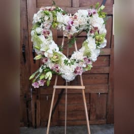 Heart-shaped floral wreath of white roses and orchids on an easel