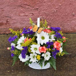 Basket of white daisies, purple statice, and pink carnations with a butterfly pick