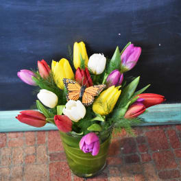 Colorful tulip bouquet in a green glass vase with a butterfly accent