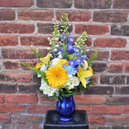 Mixed bouquet of yellow, blue, and white flowers in a blue vase