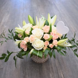 Low floral arrangement of white roses, lilies, and peach spray roses in a patterned vase