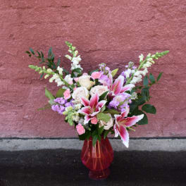 Bouquet of pink lilies, white roses, and purple flowers in a red glass vase