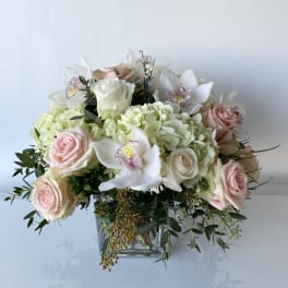 Bouquet of pale pink roses, white orchids, and green hydrangeas in a glass vase