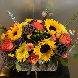 Bright mixed bouquet with sunflowers, roses, and lotus pods in a rustic container
