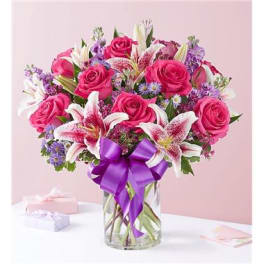 Pink roses and lilies in a clear glass vase with a purple ribbon