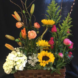 Mixed flower arrangement in a woven basket with lilies, roses, sunflowers, and hydrangea