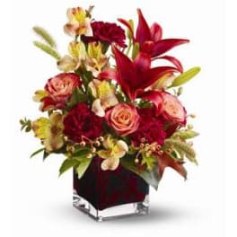 Red lilies and roses arranged in a square glass vase