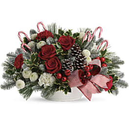 Christmas arrangement with red roses, white blooms, candy canes, and pinecones in a white bowl