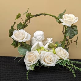 White roses arranged around a small angel figurine in a decorative container