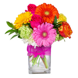 Colorful bouquet of gerbera daisies and roses in a glass vase with a pink ribbon