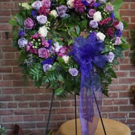 Large floral wreath with purple roses and a sheer purple bow on a stand