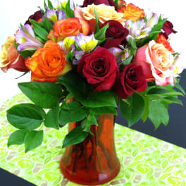 Bouquet of red, orange, and peach roses with alstroemeria in an orange glass vase