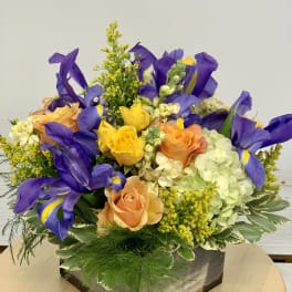 Mixed bouquet of purple irises, roses, and hydrangeas in a wooden box