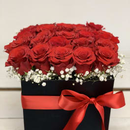 Red roses arranged in a black box with a red ribbon and white baby's breath