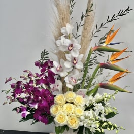 Tropical arrangement with orchids, roses, and bird of paradise in a white vase