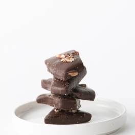 Stack of dark chocolate bark pieces with nuts on a small white plate