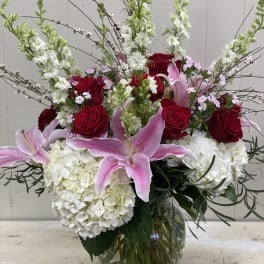 Bouquet of red roses, pink lilies, and white hydrangeas in a glass vase
