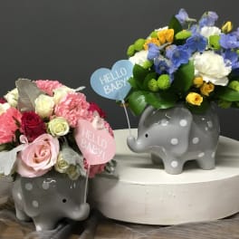Two polka dot elephant vases filled with mixed pastel flowers and Hello Baby heart picks.