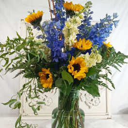 Tall bouquet of sunflowers and blue delphinium in a glass vase